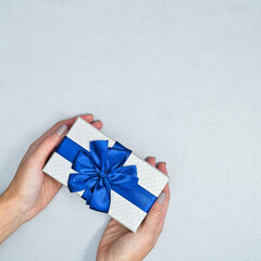 Woman hands hold silver gift with blue ribbon. Christmas and holidays concept. Flat lay