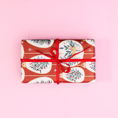 Christmas gift with red ribbon on pastel pink backgrund. Flat lay winter holidays concept