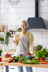 beautiful elderly gray haired senior woman cook in cozy kitchen with fresh organic vegetables on...