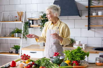 beautiful elderly grey haired senior woman in cozy kitchen takes vitamin supplement in capsule, drinks pure water from glass, biologically active food additives for full life, healthy food active life