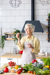 beautiful elderly grey haired senior woman in cozy kitchen takes vitamin supplement in capsule,...