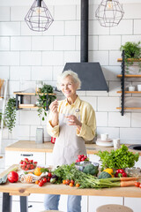 beautiful elderly grey haired senior woman in cozy kitchen takes vitamin supplement in capsule, drinks pure water from glass, biologically active food additives for full life, healthy food active life