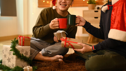 Two happy men clinking cups of hot chocolate while celebrating Christmas or New Year together in...