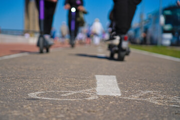 Fototapeta premium A bike path with markings and scooters passing along it. Scooters on the bike path. Rest on a scooter in the city center. Sports leisure.