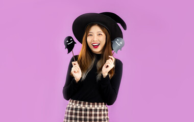 Halloween theme, young asian girl in black costume wearing witch hat posing enjoying on purple color background.
