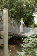 a girl in a white dress with black polka dots on a hanging bridge in the city of Mariinsky Posad