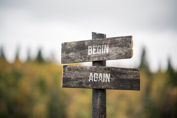 vintage and rustic wooden signpost with the weathered text quote begin again, outdoors in nature. blurred out forest fall colors in the background.