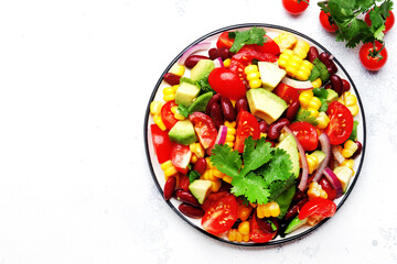 Mexican spicy salad with corn, red beans, avocado, jalapeno, tomatoes, onion and cilantro. White stone table background, top view