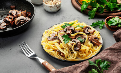 Tasty tagliatelle pasta with mushrooms served on plate with parsley and spices on grey stone kitchen table background, top view. Healthy vegan cooking and eating. Italian food concept