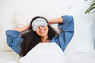 A young multi-ethnic woman stretches with arms behind head and sleep mask