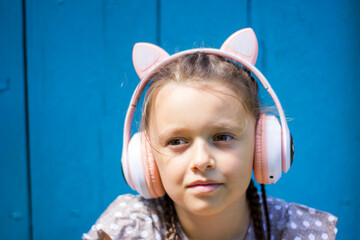 Cute little girl with wireless headphones listening to music on blue wooden background.