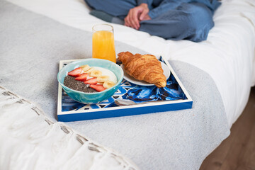 Close up of breakfast tray with croissant, fruit bowl on bed with woman sitting
