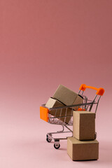 Composition of shopping cart with boxes on pink background