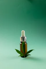 Poster Vertical image of bottle of cbd oil and marihuana leaf on green surface © vectorfusionart
