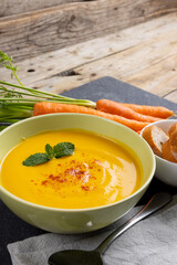 Vertical image of bowl of carrot soup with garnish, carrots and sliced bread on wood, copy space
