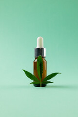 Vertical image of bottle of cbd oil and marihuana leaf on green surface