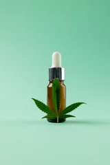 Foto op Plexiglas Vertical image of bottle of cbd oil and marihuana leaf on green surface © vectorfusionart