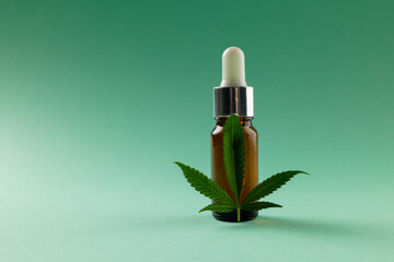 Image of bottle of cbd oil and marihuana leaf on green surface
