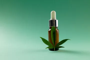 Foto op Aluminium Image of bottle of cbd oil and marihuana leaf on green surface © vectorfusionart