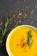 Vertical image of bowl of carrot soup with rosemary garnish, and seeds on slate, copy space
