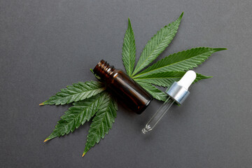 Image of marihuana leaf and bottle of cbd oil on grey surface