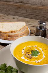 Vertical image of bowl of carrot soup with garnish, pepper and sliced bread on wood, copy space
