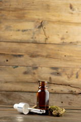 Vertical image of bottle of cbd oil and dried marihuana leaves on wooden surface