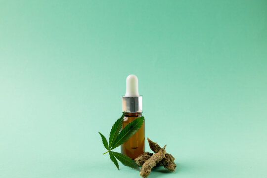 Image of bottle of cbd oil and dried marihuana leaves on green surface