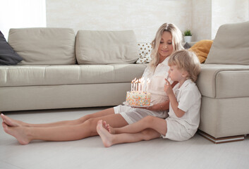 Happy woman and boy celebrating the child birthday at home. The kid blows out the candles in the...