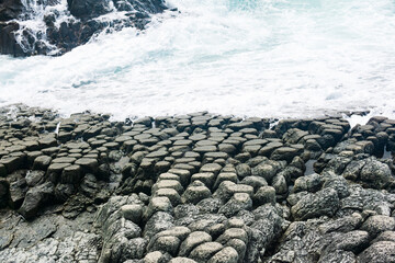 natural cobblestone causeway, formed by the ends of lava columns, descends into the sea surf