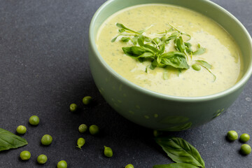 Horizontal image of bowl of pea soup with garnish, and peas on slate, copy space