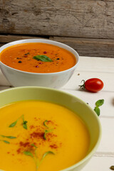Vertical image of bowls of carrot and tomato soups on white wood, with copy space
