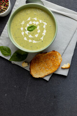 Vertical image of bowl of pea soup, with toast and peppercorns on slate, with copy space