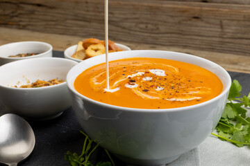 Horizontal image of cream pouring into bowl of tomato soup, with toast and leaves