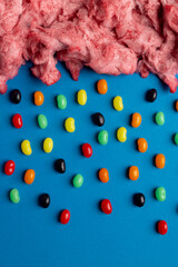 Vertical image of cloud of homemade pink candy floss raining jelly beans, on blue with copy space