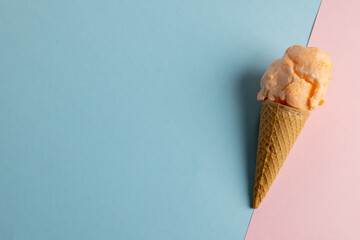 Horizontal image of orange homemade ice cream in cone, on blue and pink with copy space