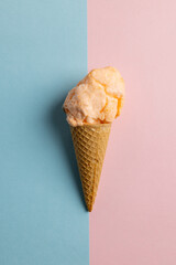 Vertical image of orange homemade ice cream in cone, on blue and pink with copy space