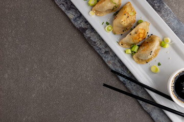 Overhead view of dumplings, soy sauce and chopsticks on grey background