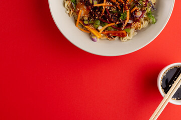 Overhead view of asian wok stir fry, soy sauce and chopsticks with copy space on red background