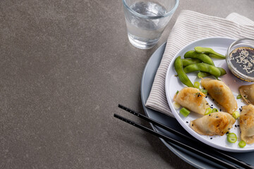 Overhead view of asian dumplings, soy sauce and chopsticks with glass of water on grey background