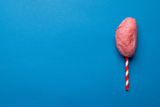 Horizontal image of homemade pink candy floss on striped stick, on blue background with copy space