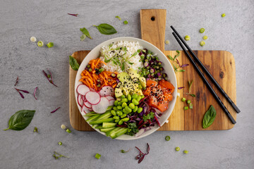 Overhead view of hawaiian poke bowl with chopsticks on wooden chopping board and grey background