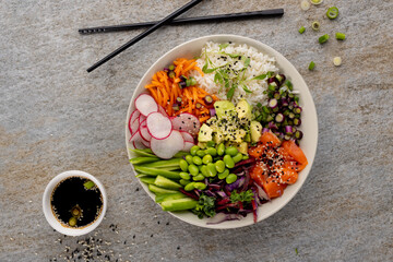 Overhead view of hawaiian poke bowl with chopsticks and soy sauce on grey background