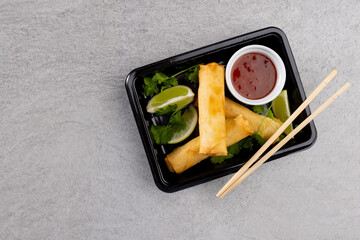 Overhead view of asian spring rolls, sliced lime, chilli sauce and chopsticks on grey background