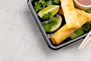 Overhead view of asian spring rolls, sliced lime, chilli sauce and chopsticks on grey background