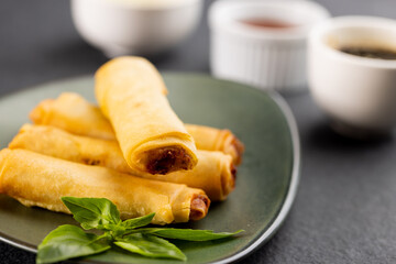 Close up of asian spring rolls on grey plate and condiments on grey background