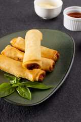 Close up of asian spring rolls on grey plate and condiments on grey background