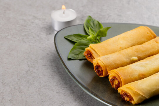 Overhead view of asian spring rolls on grey plate and lit tea candle on grey background