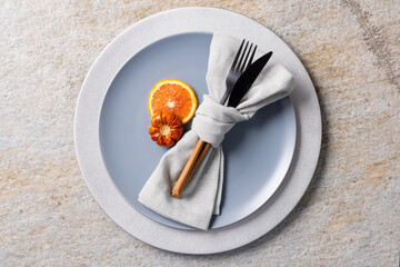 Overhead view of plate and cutlery with autumn decoration and copy space on grey background
