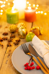 Overhead view of plate and cutlery with autumn decoration and candles on wooden background